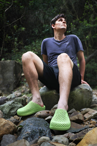 Person wearing green textured shoes sitting on rocks in a natural setting